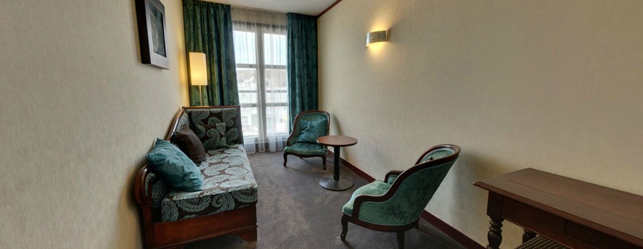A hotel room with a sofa, two armchairs, a small table, and a lamp.