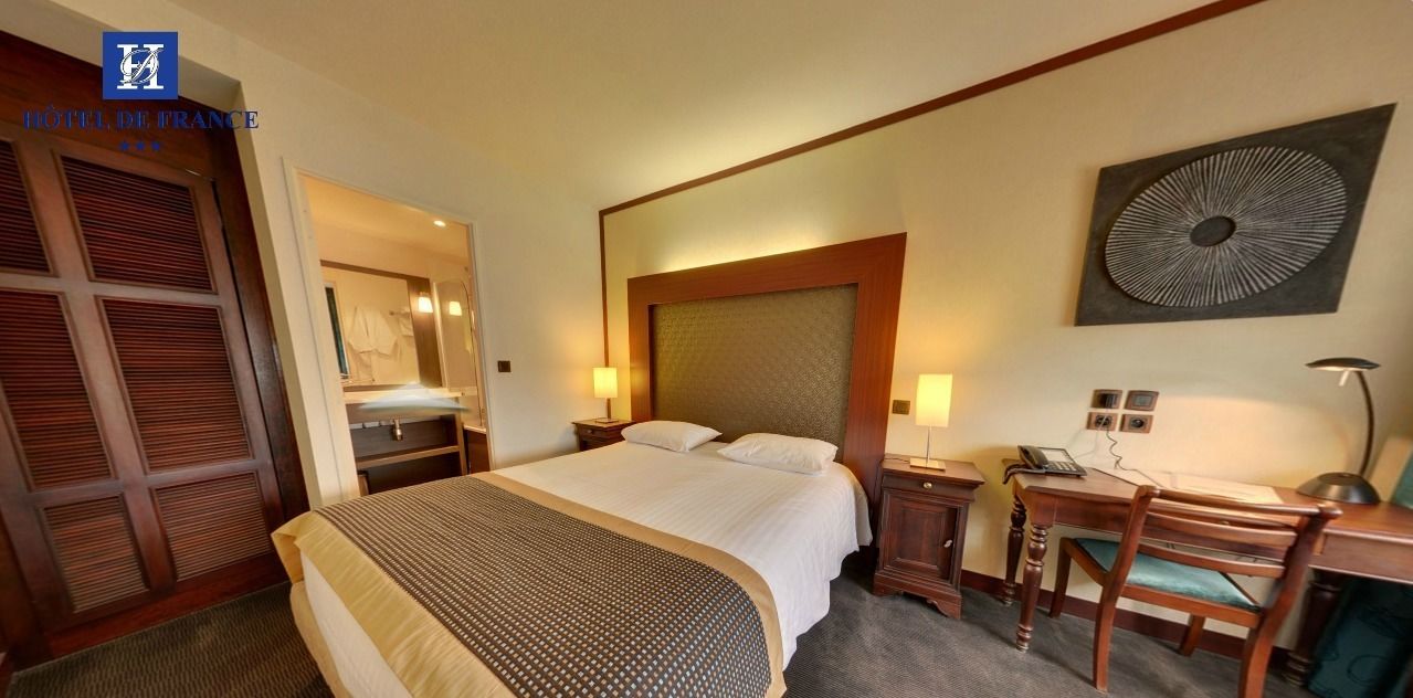 A hotel room with a large bed, a desk with a chair, a wardrobe, and a wall-mounted artwork.