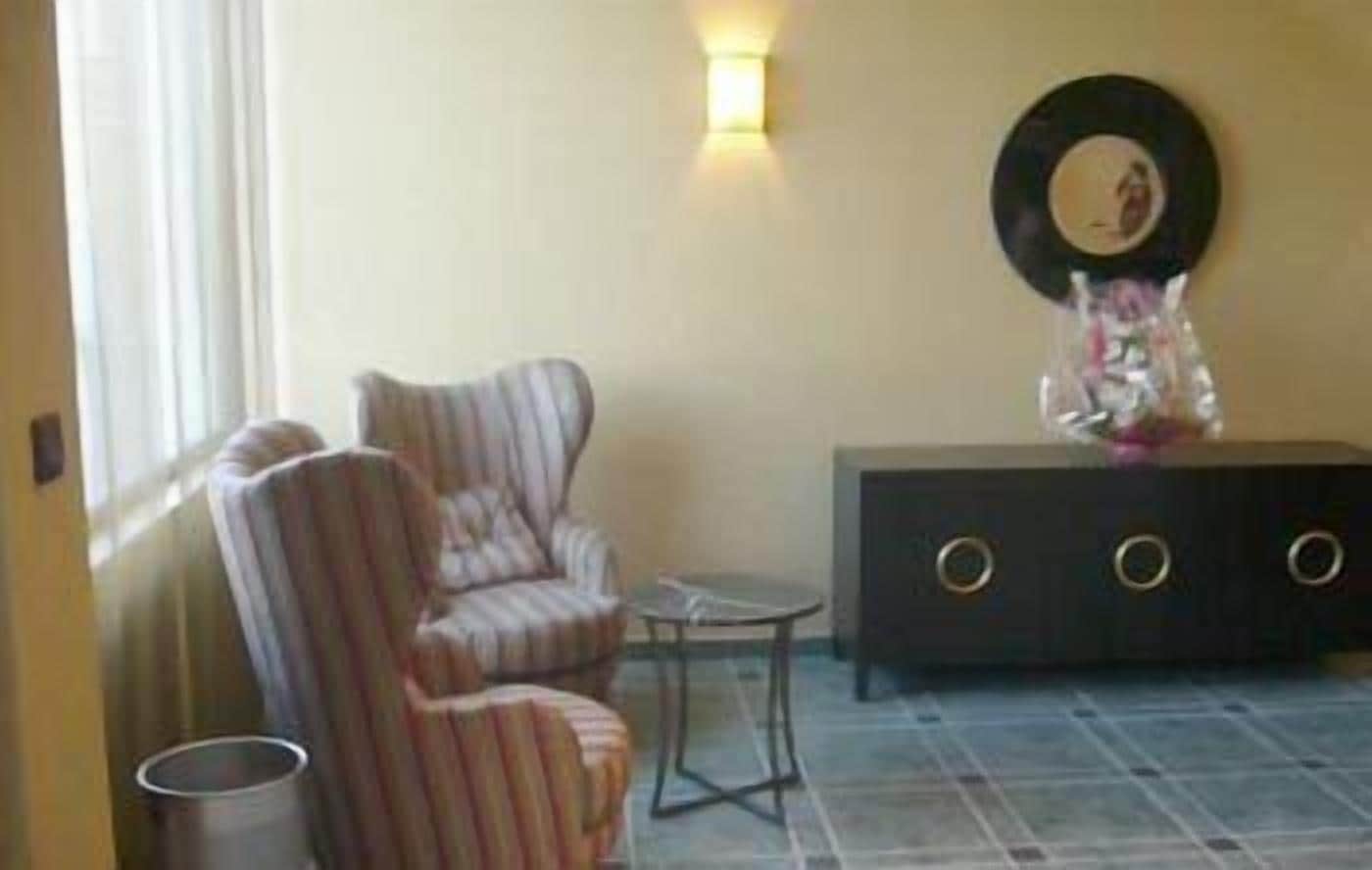Una habitación con un sillón a rayas, una mesita pequeña y un mueble oscuro con un objeto decorativo encima.