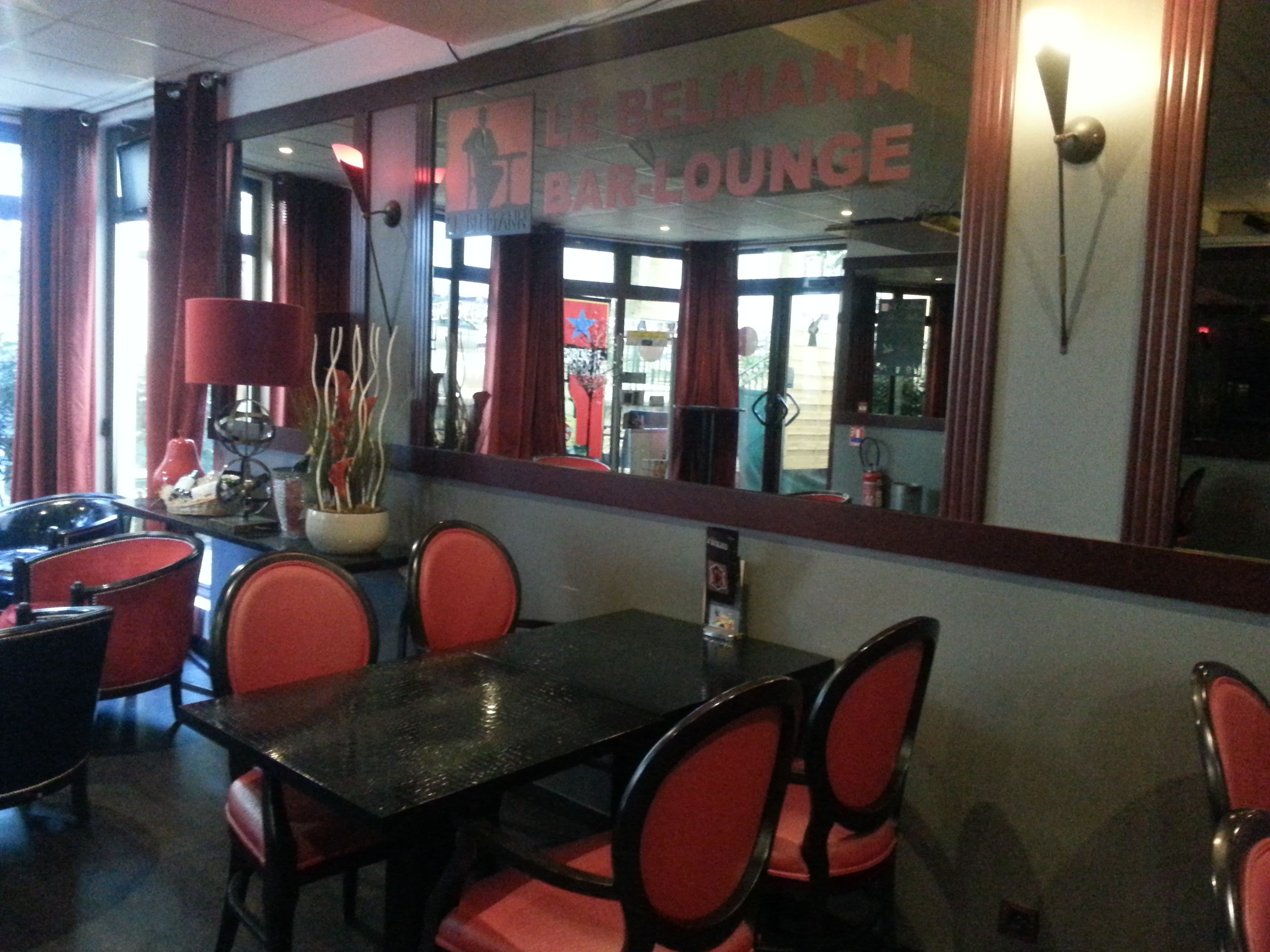 A restaurant interior with a bar/lounge area, red chairs, a black table, and a large mirror reflecting the interior.