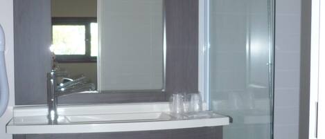 Un baño con tocador de madera oscura, un espejo grande, cabina de ducha de vidrio y una toalla blanca colgada en la puerta.