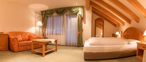 Una habitación de hotel con cama, sofá, una mesita y ventana con cortinas.