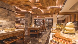 Une boulangerie aux plafonds en bois et aux murs en pierre, où une variété de pâtisseries et de desserts sont présentés sur des tables.