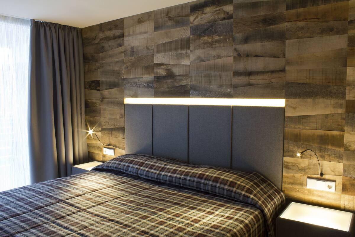 A modern bedroom with a wooden headboard, a plaid bedspread, and bedside lamps.