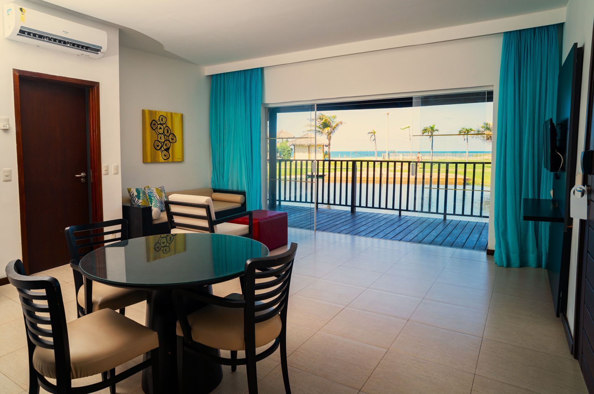 Una habitación con una mesa redonda y sillas, un sofá, un televisor y un balcón con vista al mar.
