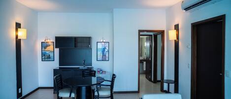 A modern living room with a dining area, a flat-screen TV, and a built-in air conditioner.