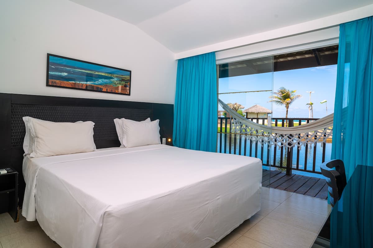 A hotel room with a large bed, a view of the sea, and a hammock on the balcony.