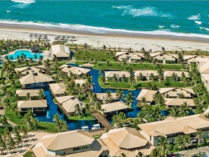 A resort with multiple bungalow-style buildings, a central swimming pool, and a beach view. - Dom Pedro Laguna Beach Resort & Golf by WAM Experience (Aquiraz)