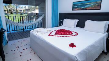 Habitación de hotel con cama, hamaca, balcón con vista al océano y un cuadro en la pared.