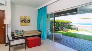 Un soggiorno moderno con un divano, un poggiapiedi rosso e una porta vetrata che dà su un balcone con vista sull'oceano e una piscina.