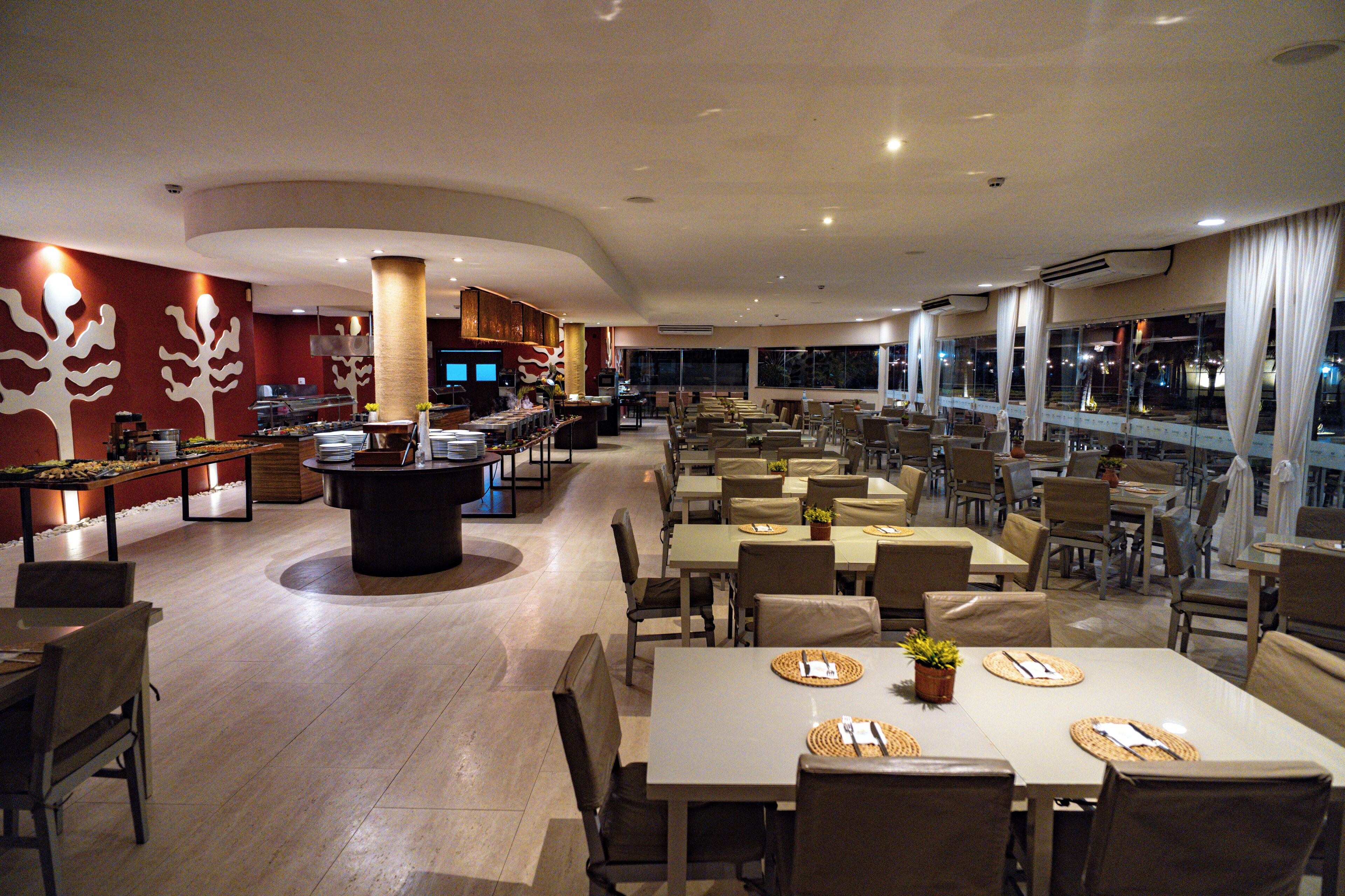 Un restaurante espacioso con varias zonas de comedor, un bar central y amplios ventanales con vistas.