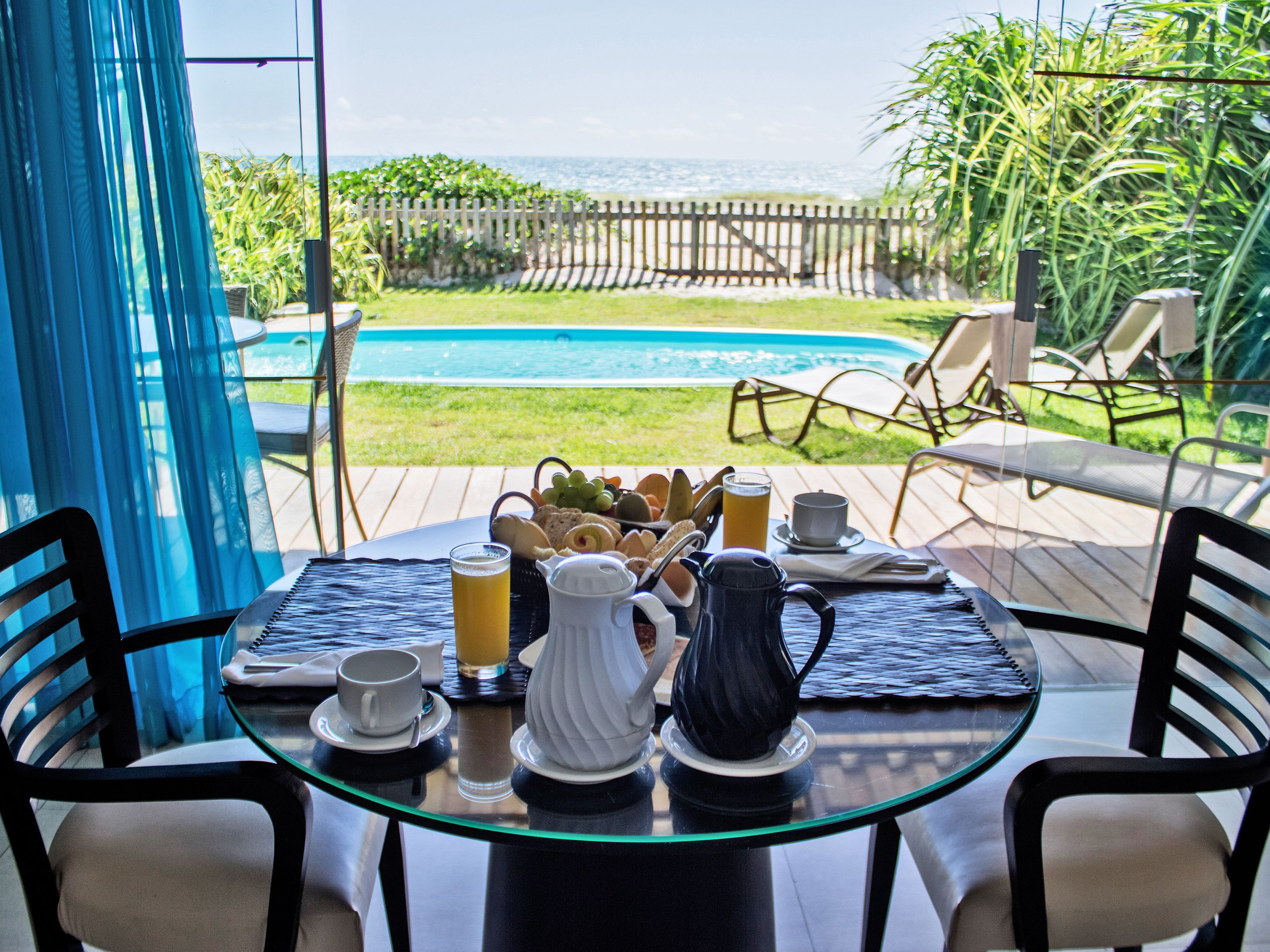Mesa posta para o café da manhã, com vista para a piscina e jardim.