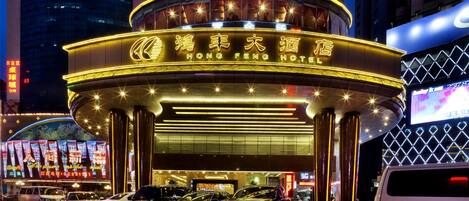 Exterior del hotel Hong Feng con un cartel iluminado llamativo, una entrada curva y varios coches aparcados en la parte delantera.