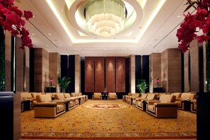 A spacious lobby with a large, ornate chandelier, a patterned carpet, and several seating areas.
