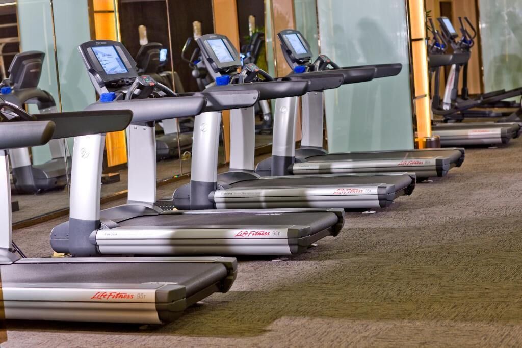 Una hilera de cintas de correr en un gimnasio con paredes de espejo.