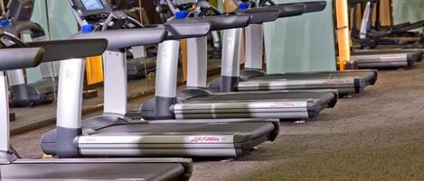 Una hilera de cintas de correr en un gimnasio con paredes de espejo.