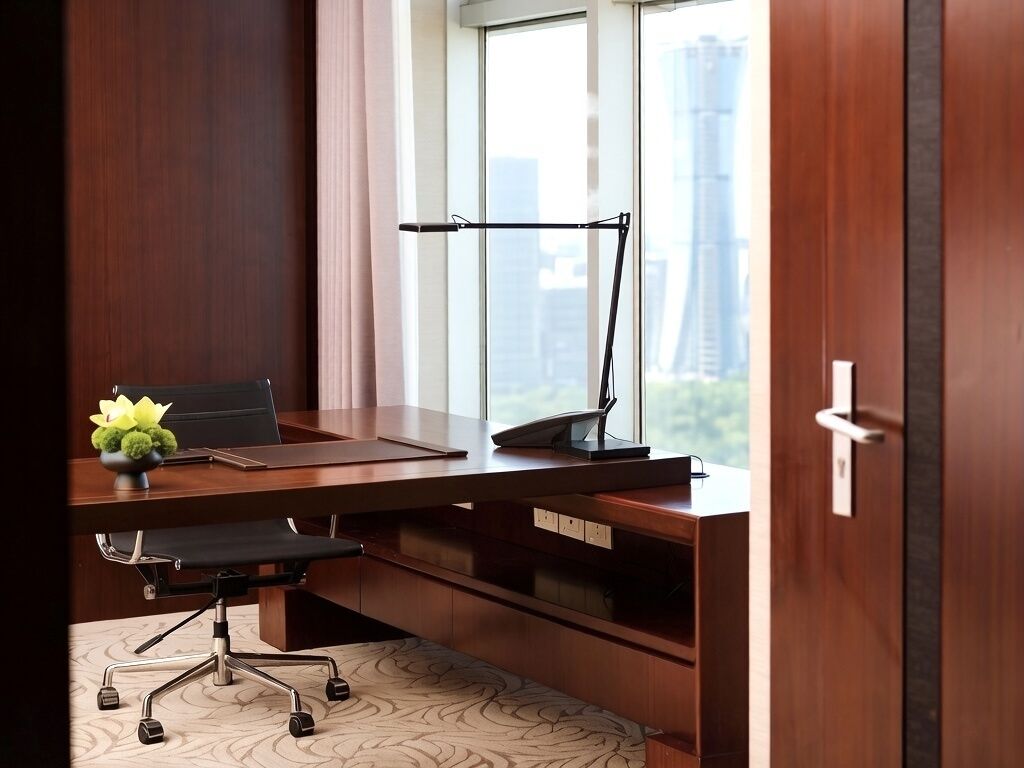 A modern office desk with a laptop, phone, and decorative plant, positioned near a window with a city view.