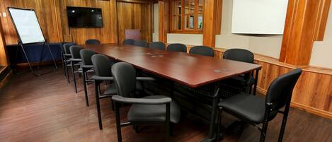A conference room with a long wooden table, black chairs, a whiteboard, and a projector screen.