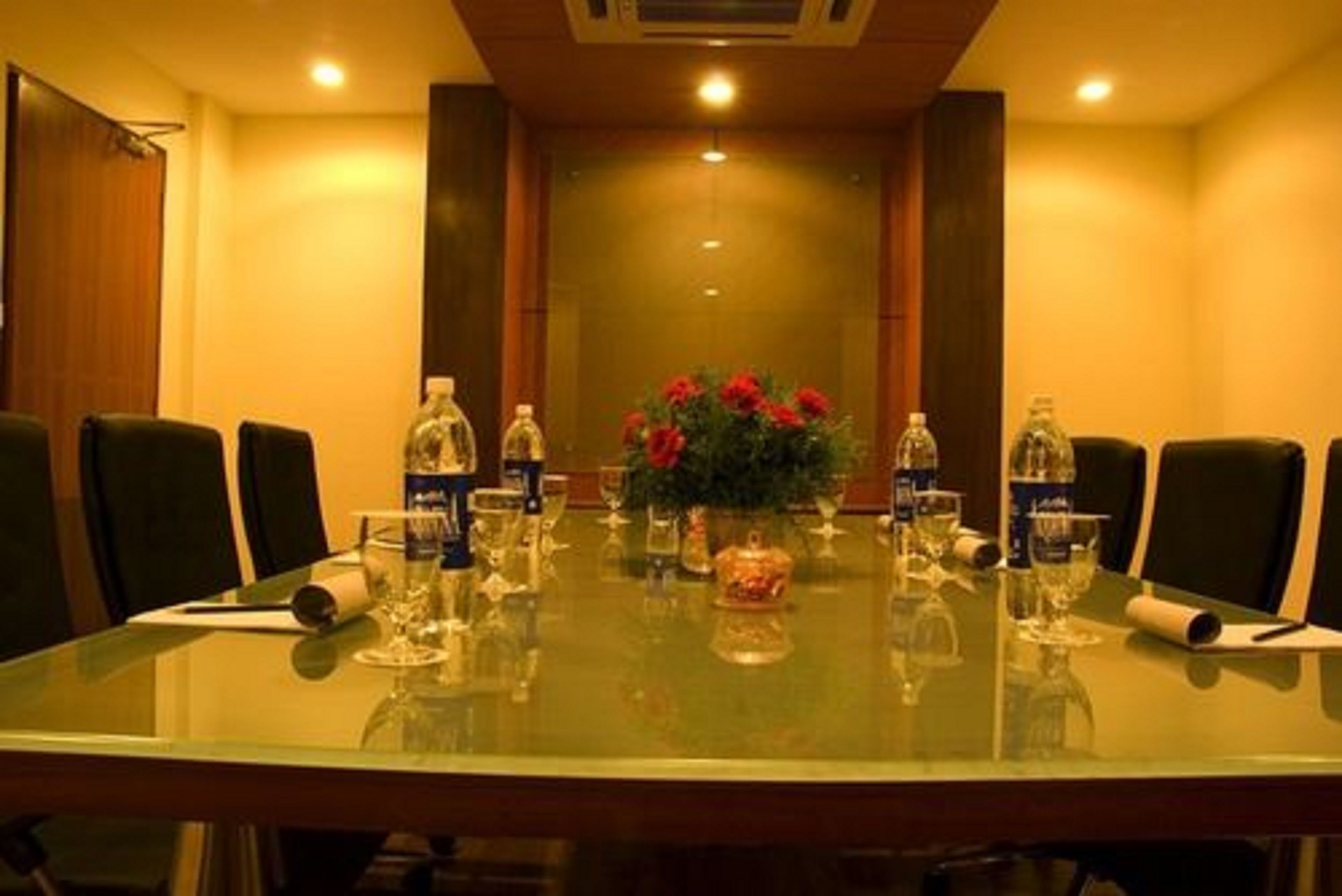 A conference room with a glass table, chairs, water bottles, and a vase with flowers.