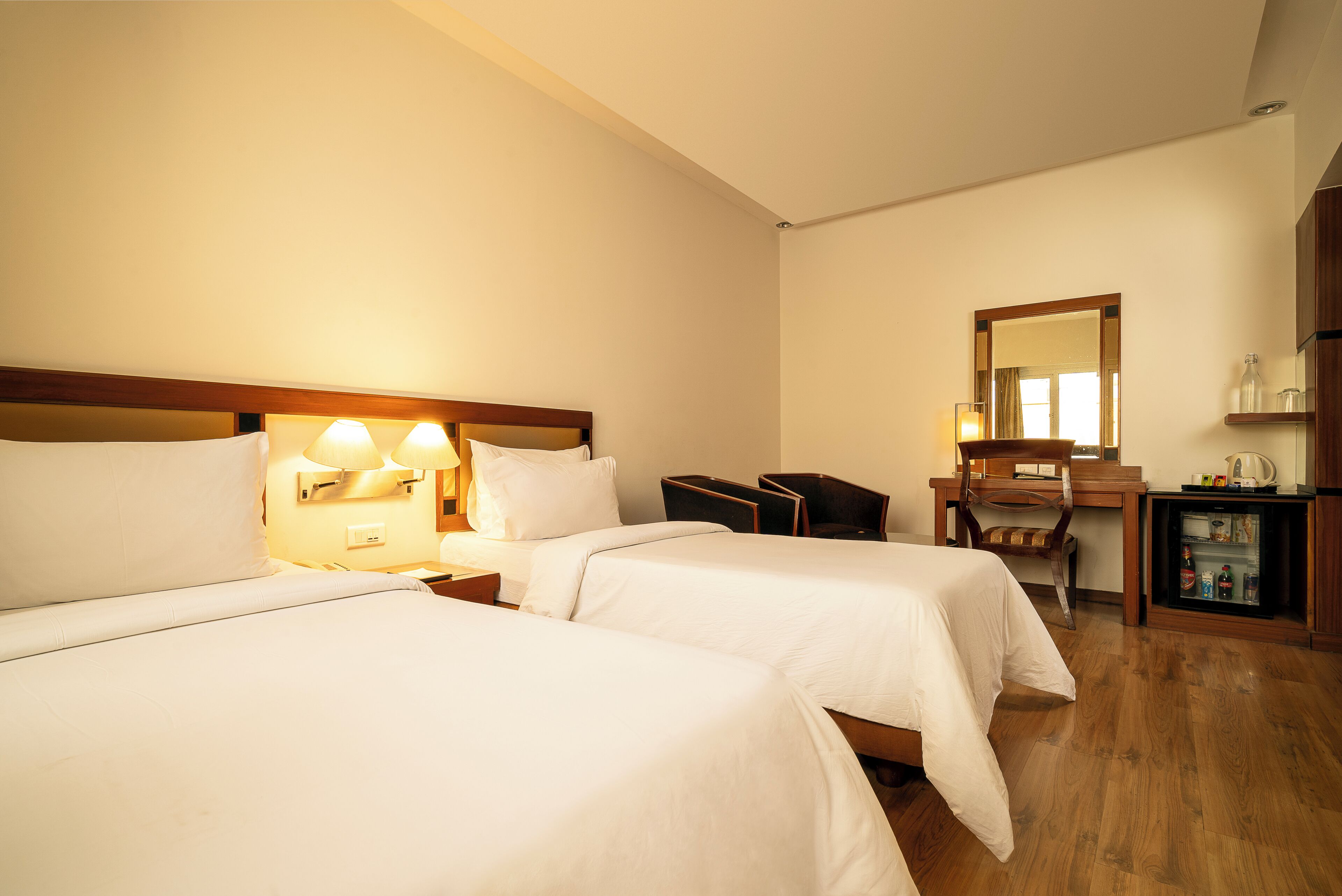 Habitación de hotel con dos camas, un escritorio, una silla, un espejo y un minibar.