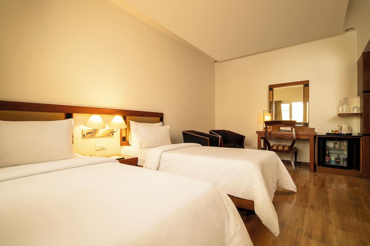 Habitación de hotel con dos camas, un escritorio, una silla, un espejo y un minibar.