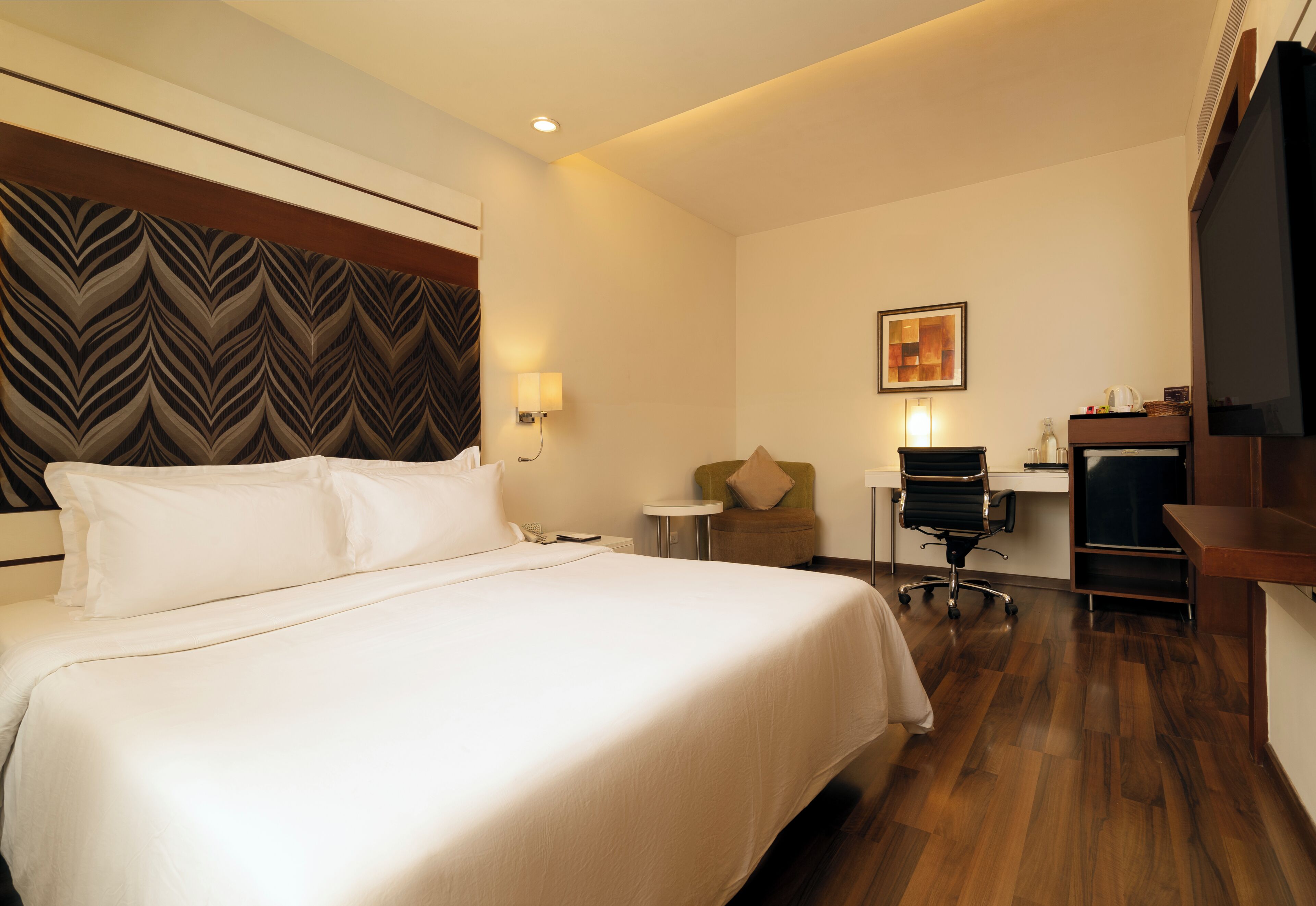 Habitación de hotel con una cama grande, un escritorio, una silla, un televisor y una obra de arte en la pared.