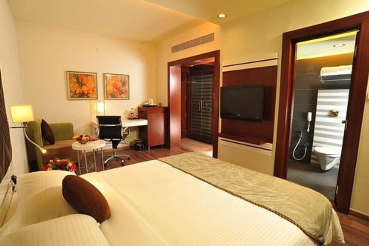 A hotel room with a bed, desk, chair, TV, and a bathroom visible through an open door.