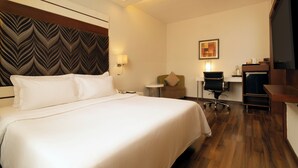 Habitación de hotel con una cama grande, un escritorio, una silla, un televisor y una obra de arte en la pared.