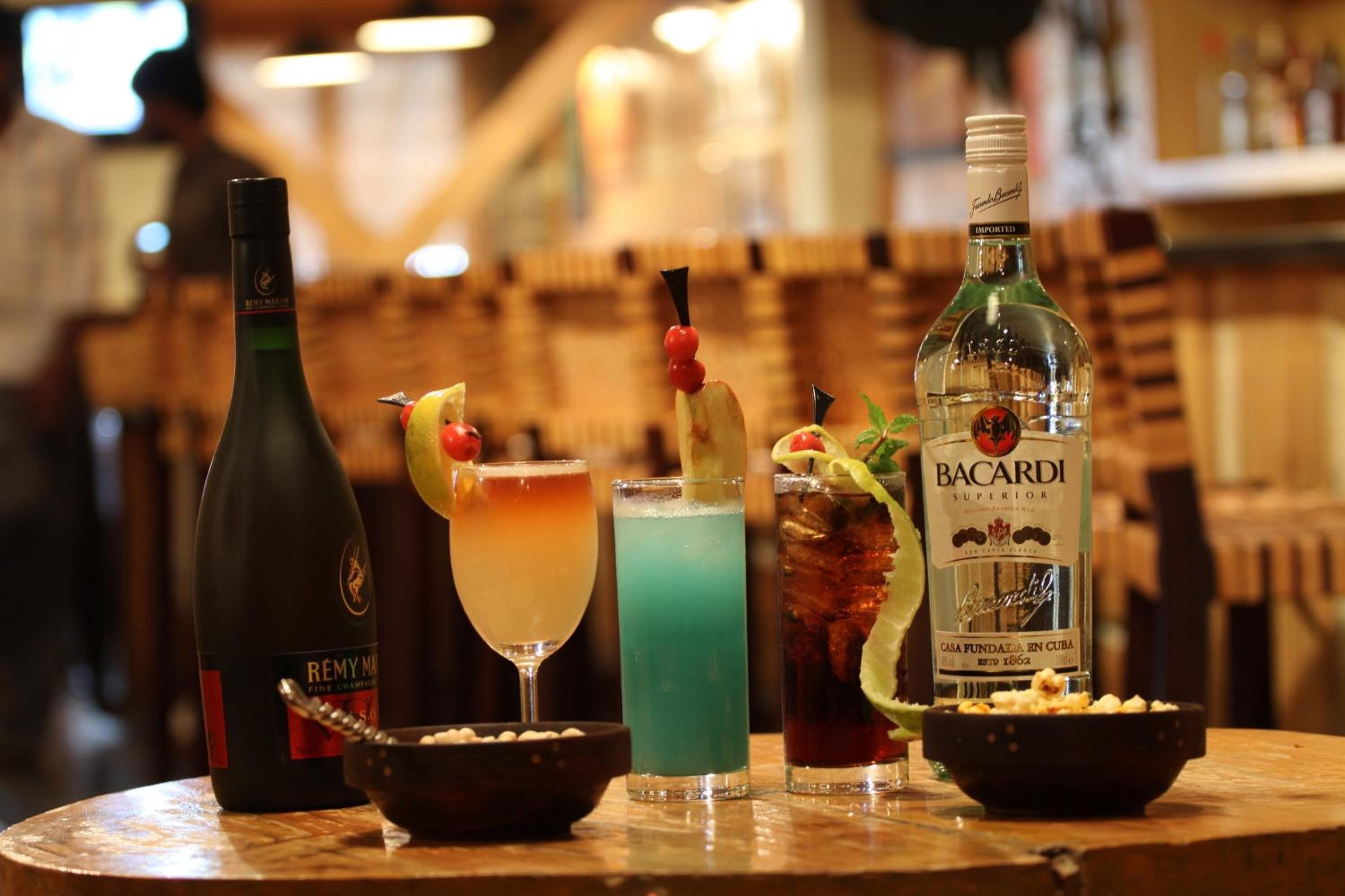 Un bar con una botella de Rémy Martin, Bacardí Superior y tres cócteles.