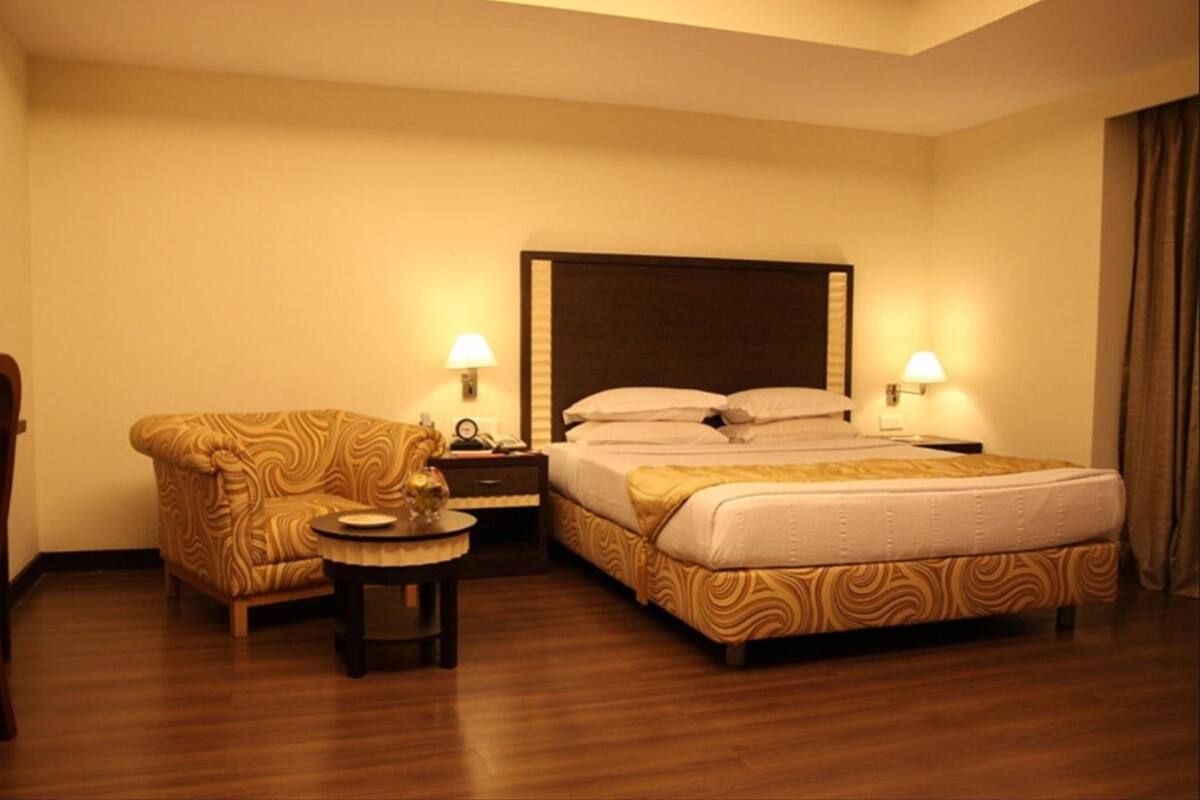 A hotel room with a bed, a sofa, two bedside tables, and lamps.