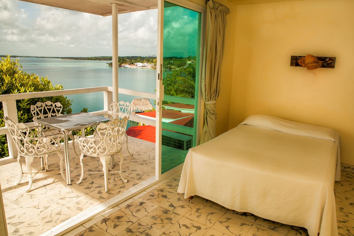 A balcony with a table and chairs, a bed, and a view of the sea.