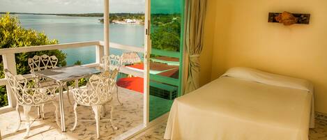 A balcony with a table and chairs, a bed, and a view of the sea.
