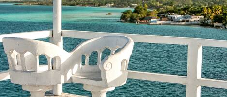 Two white chairs on a balcony overlooking a body of water with a distant shoreline.