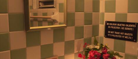 Un baño con pared de baldosas a cuadros, un lavamanos, un espejo, una vela y un florero con flores.