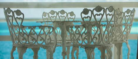A white metal outdoor table and chairs with intricate designs, positioned near a window overlooking a body of water.