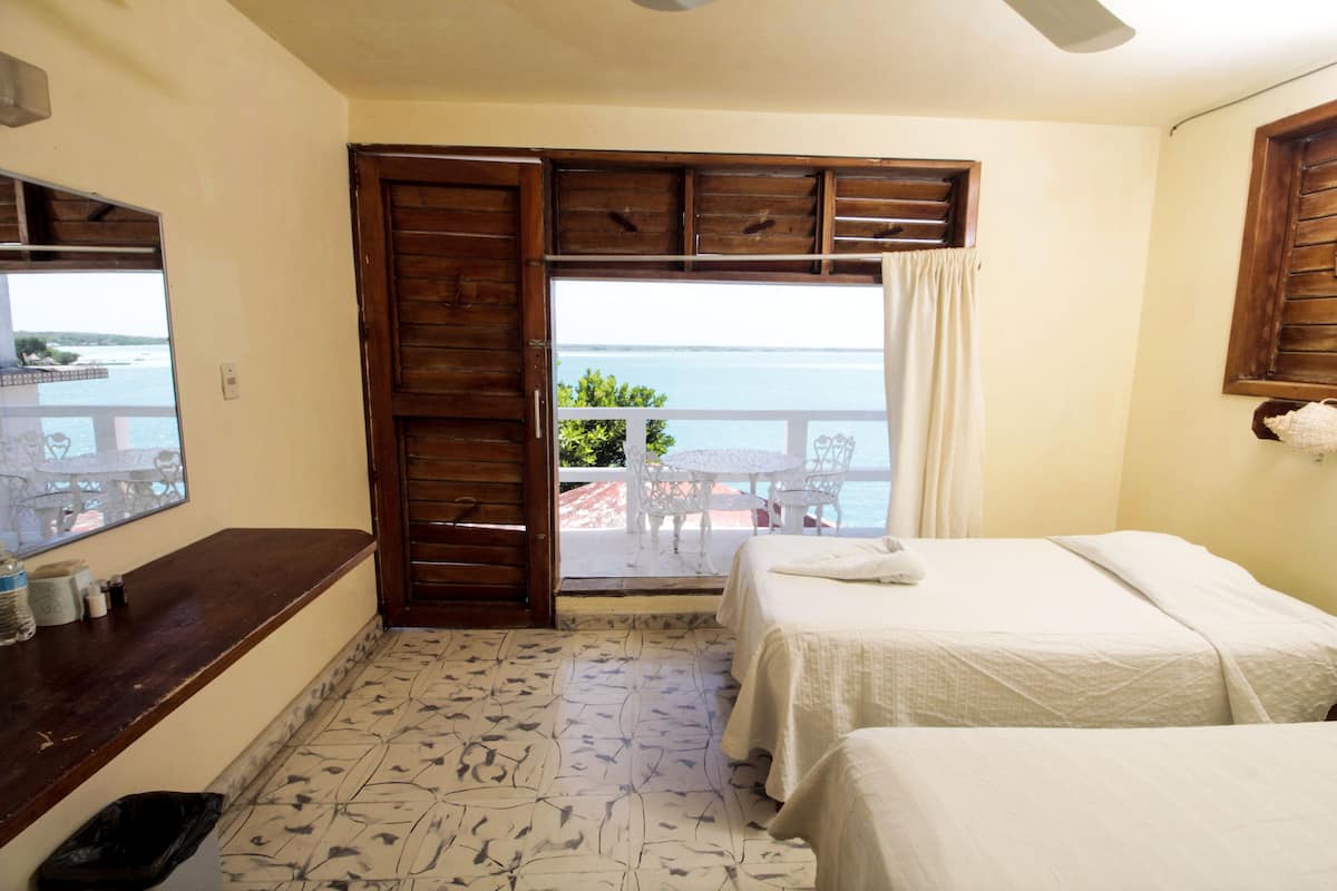A room with two beds, a wooden counter, and a view of the sea through a large window.