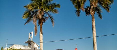 Una entrada protegida con un arco decorativo, palmeras y un edificio con techo rojo.