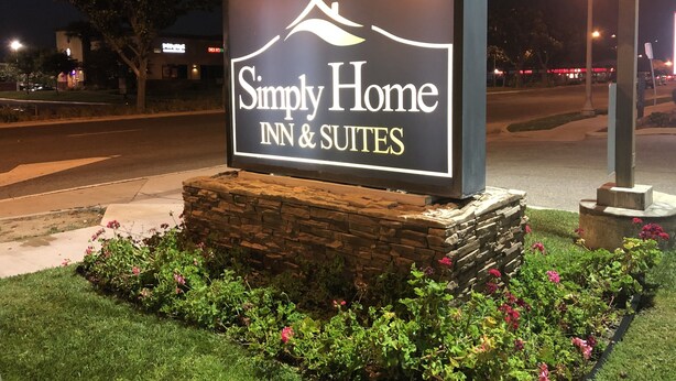 A sign for Simply Home Inn & Suites with a stone base and a landscaped garden. - Simply Home Inn & Suites (Riverside)