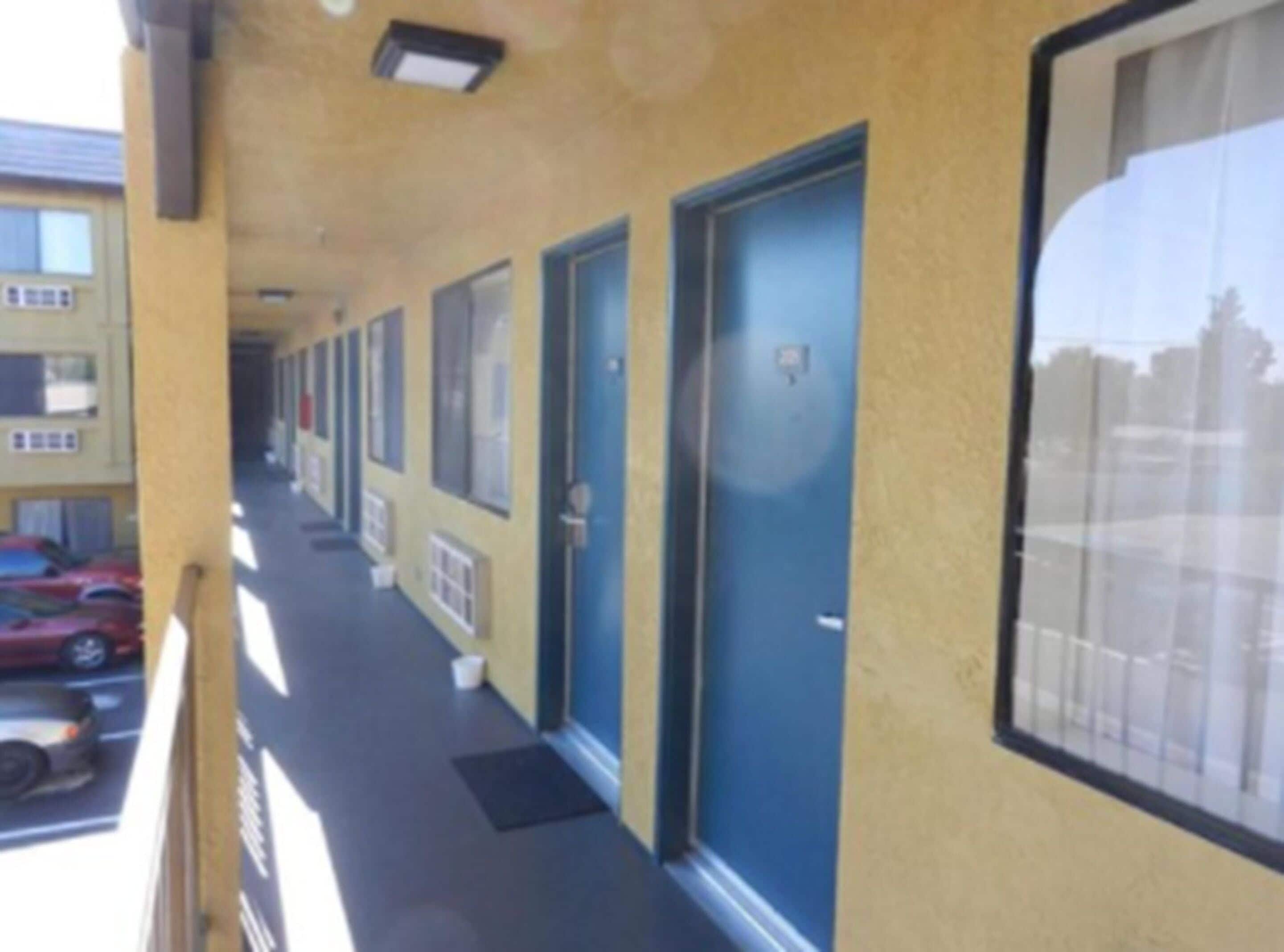 Une rangée de portes bleues sur un bâtiment jaune, avec un parking visible à l’arrière-plan.