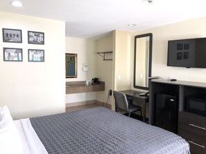 A hotel room with a bed, a desk, a chair, a TV, a mirror, and pictures on the wall.