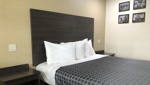 A neatly made bed with white pillows and a patterned bedspread, a dark headboard, and a nightstand with a power outlet. - Simply Home Inn & Suites (Riverside)
