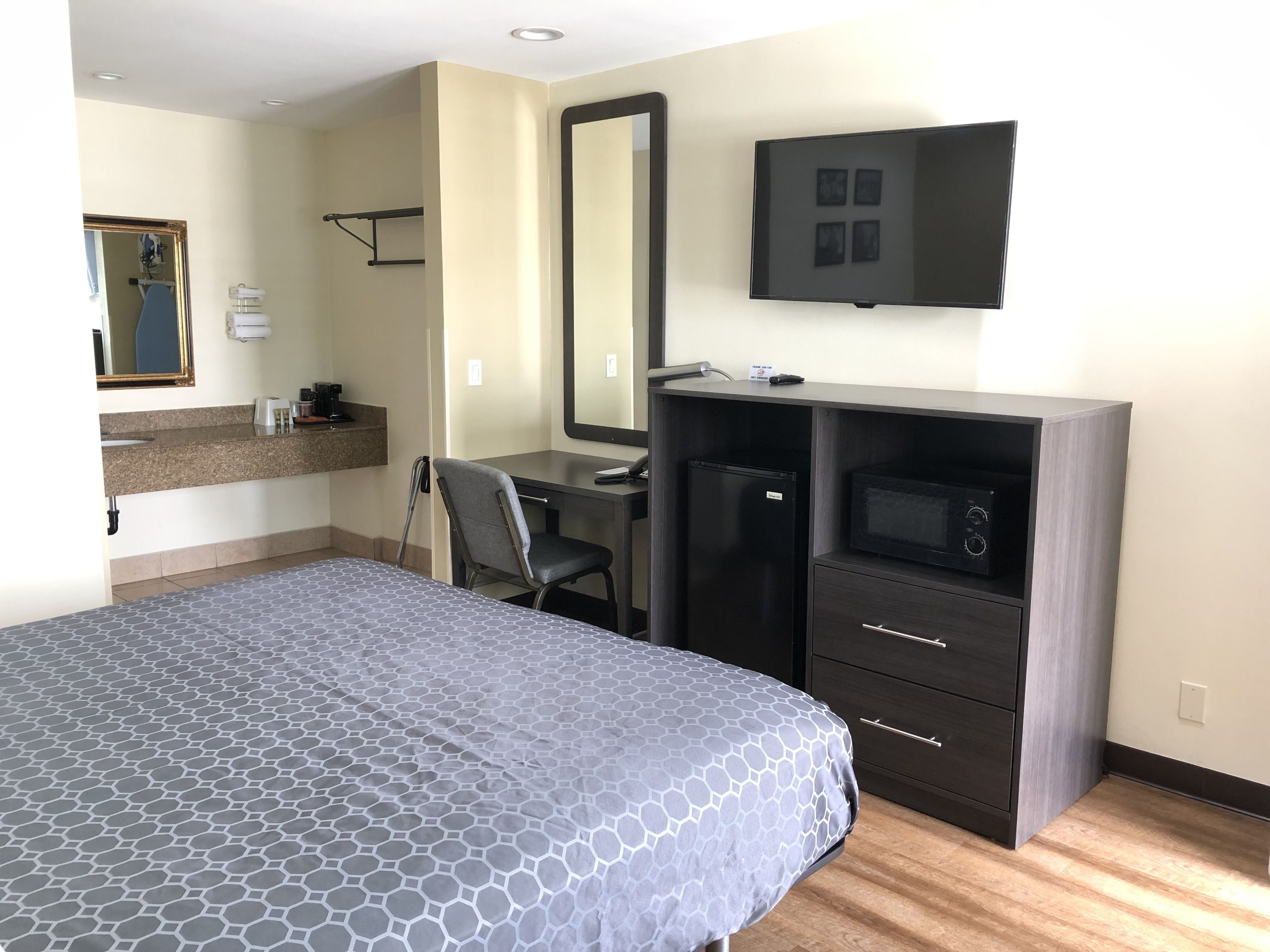 A hotel room with a bed, a desk, a chair, a mirror, a television, and a minibar.