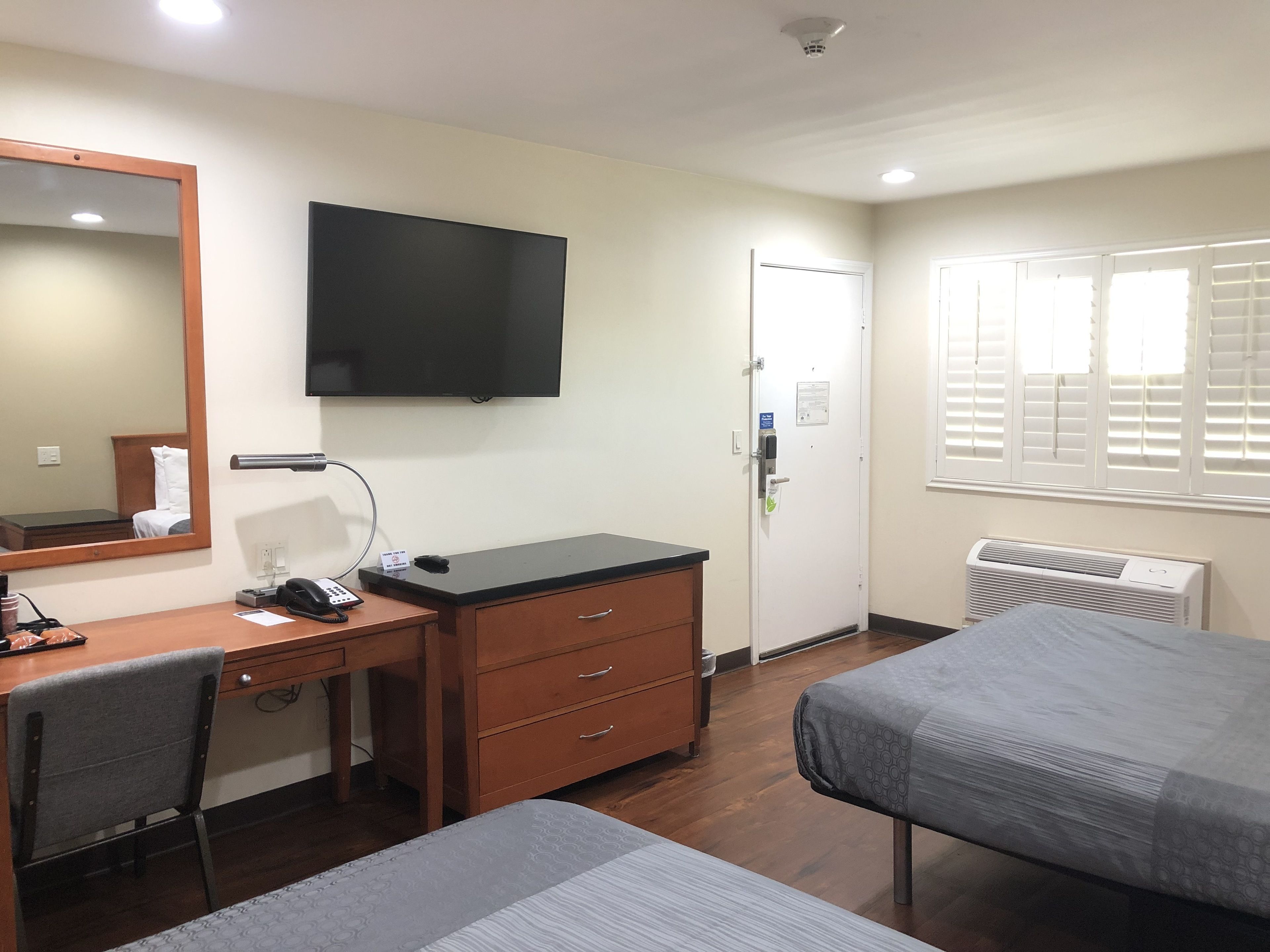 Una habitación de hotel con escritorio, silla, cama, televisor y ventana con persianas.