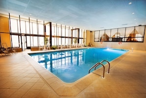 Ein Innenpool mit klaren Glaswänden, Fliesenboden und einer Poolleiter.