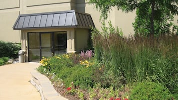 A building with a covered entrance, a landscaped garden with various plants and flowers, and a clear pathway leading to the entrance.