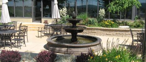 A patio area with outdoor seating, a fountain, and a building with large windows in the background.