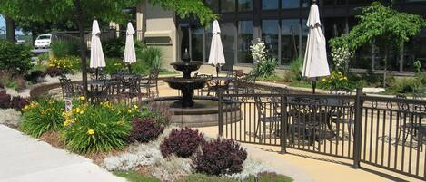 An outdoor patio area with tables and chairs, a fountain, and umbrellas.