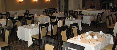 A banquet hall with multiple tables set for dining, equipped with chairs and table settings.