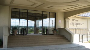 Entrada de hotel com uma escadaria imponente, uma porta de vidro grande e vista para a paisagem circundante.