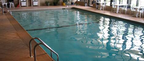 Una piscina interior con una silla de salvavidas, vestuario y una zona de estar con mesas y sillas.